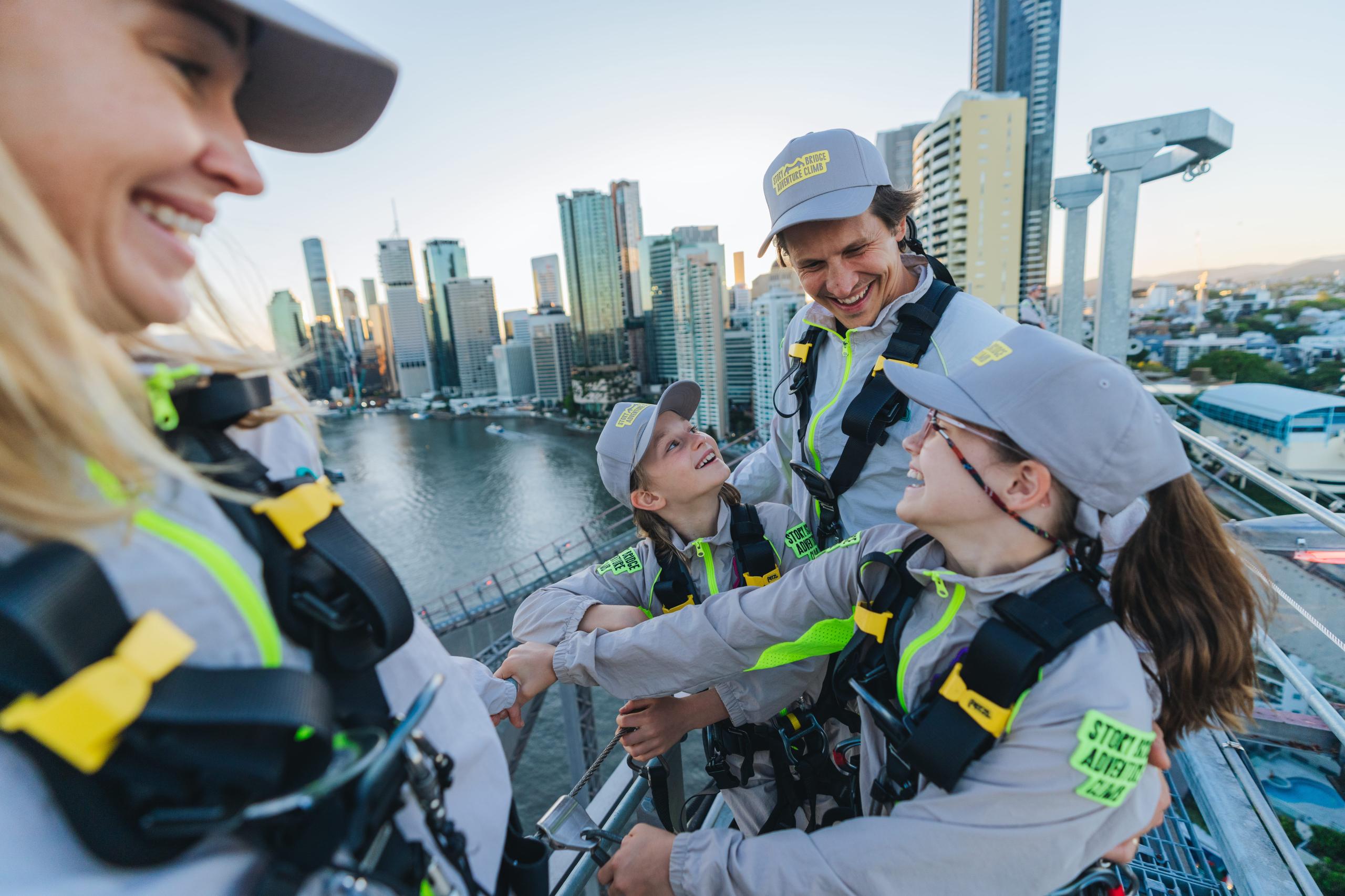 Group celebrating at the summit of Story Bridge Adventure Climb at sunset with Brisbane skyline behind them