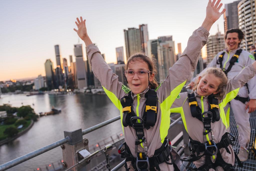 Climbers harnessed to the Story Bridge structure at sunset, well above the road deck and the Brisbane River